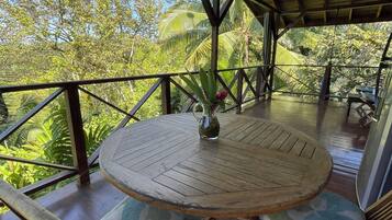 Relax in this serene outdoor seating area with a round table and two chairs, surrounded by lush greenery and palm trees.