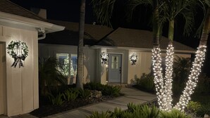Una casa residencial con un jardín delantero cuidado, que presenta un sendero hacia la entrada y luces decorativas que iluminan la puerta y las ventanas.
