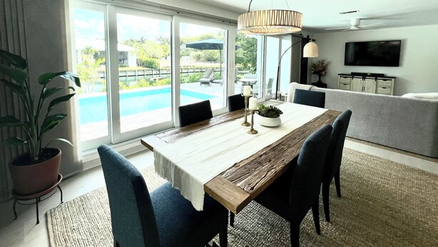 Un comedor moderno con una mesa de madera, sillas azules y vistas a una piscina a través de amplios ventanales.