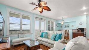 A spacious living room with a white sofa, a glass coffee table, and a ceiling fan.