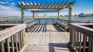 A wooden pier with a pergola structure, benches, and a view of the water and distant buildings.