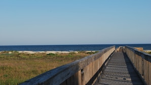 A wooden boardwalk leading to the beach with a clear view of the ocean and sandy shore.