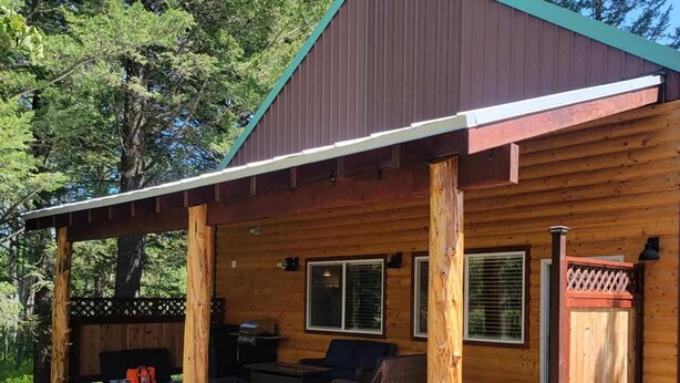 Une cabane en bois dotée d’un porche couvert, d’un espace salon extérieur et d’un coin barbecue.