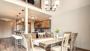 Un grand espace à manger avec une table et des chaises en bois, une cuisine à l’arrière-plan et un escalier menant à l’étage supérieur.