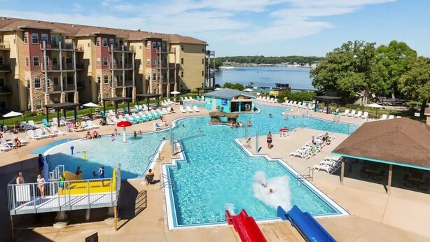 Un espace piscine doté de plusieurs toboggans, de chaises longues et offrant une vue sur un plan d’eau.