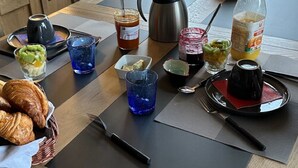Ein Frühstückstisch mit Croissants, einer Kaffeekanne, einem Thermosbehälter, einem Marmeladenglas, einem Glas Saft und einer Wasserflasche.