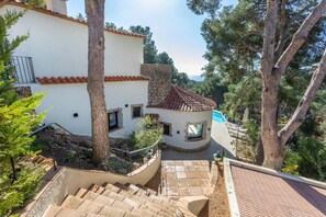 Un bâtiment blanc avec un toit recouvert de tuiles rouges, une cheminée en pierre et un petit espace piscine.