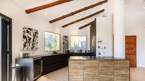 Una cocina moderna con una isla central, muebles oscuros y vigas de madera a la vista.