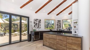 Una cocina moderna con armarios de madera, una isla grande y un puerta corrediza de vidrio que da a un área exterior con sillones.