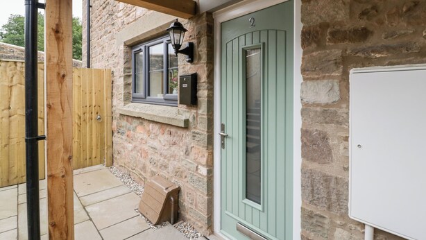 Un edificio de piedra con una puerta verde, una ventana con lámpara y una valla de madera.