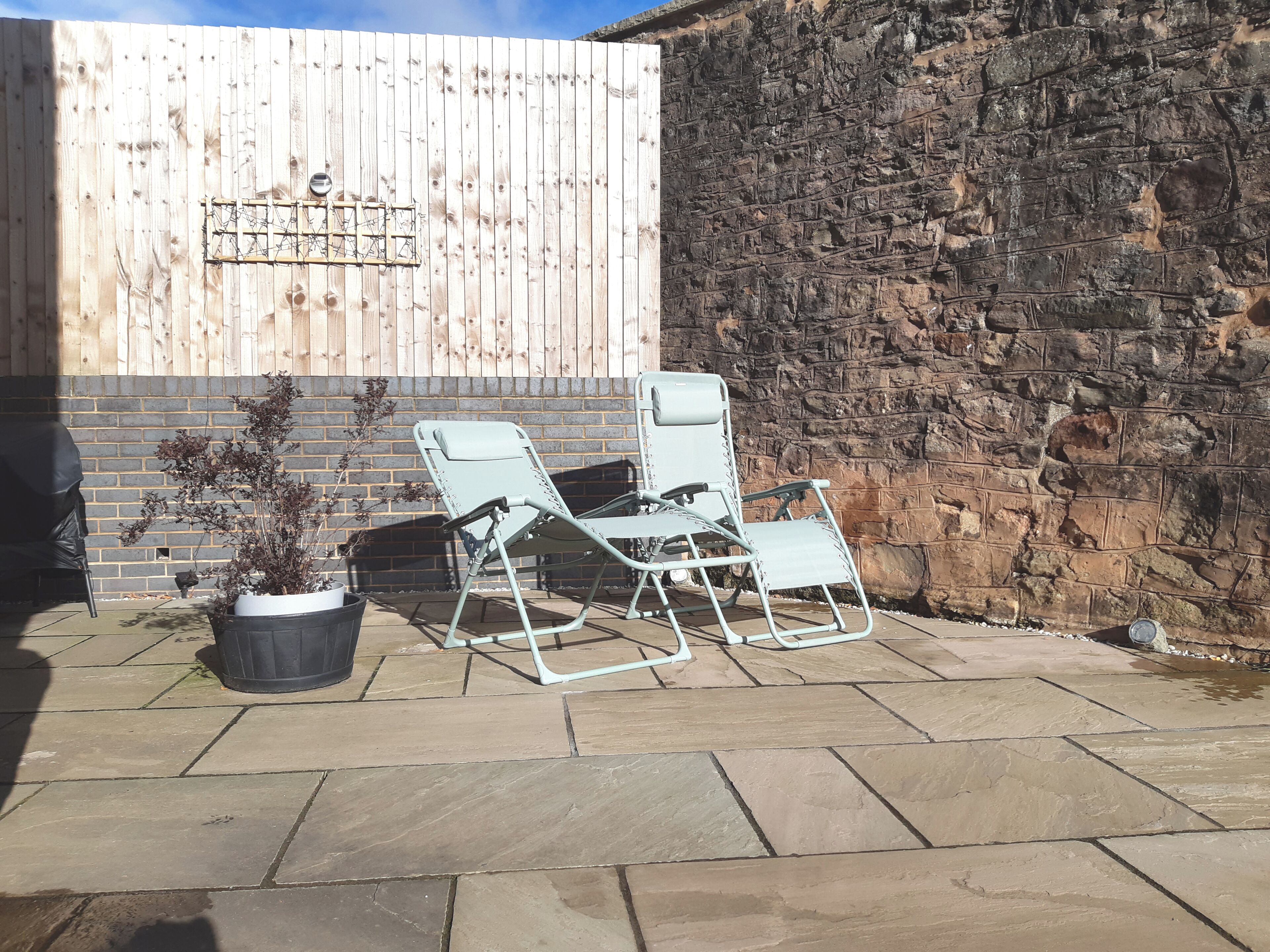A patio with two metal chairs, a potted plant, and a brick wall.