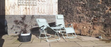 A patio with two metal chairs, a potted plant, and a brick wall.