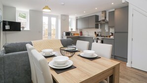 Una cocina moderna con gabinetes grises, una mesa de comedor de madera con platos blancos, y un sofá gris en la zona de estar.