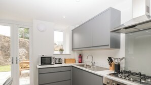 Una cocina moderna con gabinetes grises, horno empotrado, cocina a gas y ventana con vista a un jardín.