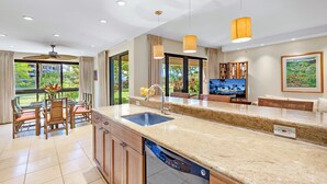 A modern kitchen with a granite countertop, built-in dishwasher, and a large window offering a view of the outdoors. - MRR Presents Kaanapali Alii 213 - Luxurious Ground Floor 3BR Interior w/ Partial Ocean Views & Lawn Area. The Pools, Beach, and BBQs are Mere Steps Away! (Lahaina)