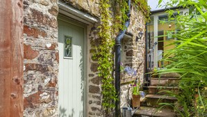 A stone building with a green door, a wooden post, and a metal gutter. - Sausage Cottage near Oakford (Nr Bampton)