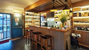 A bar area with wooden bar stools, a counter with a variety of bottles, and a large vase of flowers. - Giao Thong Hotel (Hanoi)
