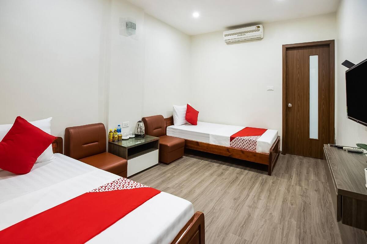 A hotel room with two beds, a desk, a chair, a TV, and an air conditioning unit.