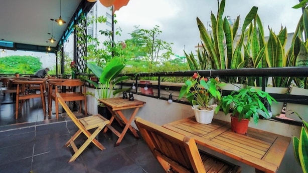 An outdoor seating area with wooden tables and chairs, potted plants, and a view of greenery. - Giao Thong Hotel (Hanoi)