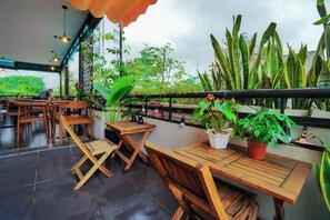 An outdoor seating area with wooden tables and chairs, potted plants, and a view of greenery. - Giao Thong Hotel (Hanoi)