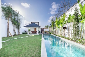 A modern outdoor pool area with a clear blue pool, a grassy lawn, and a patio with seating.