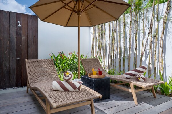 Two wicker lounge chairs with towels, a tray with drinks, and an umbrella on a wooden deck.