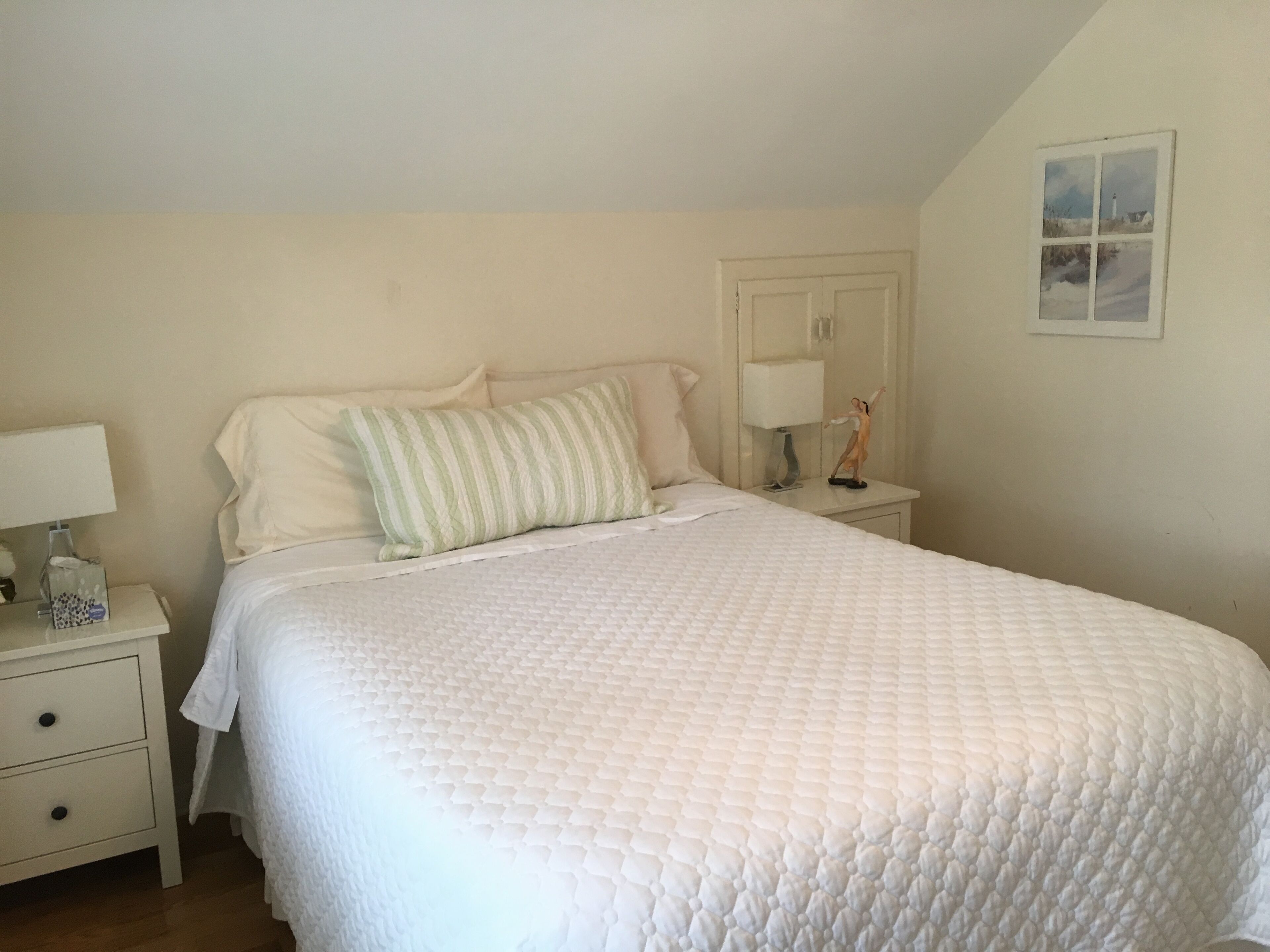 Une chambre à coucher avec un grand lit, une table de chevet avec une lampe, une commode avec des tiroirs et une étagère fixée au mur.