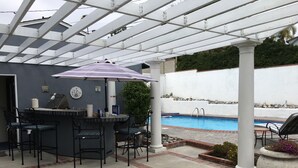 A covered patio area with a pool, outdoor seating, and a grill.