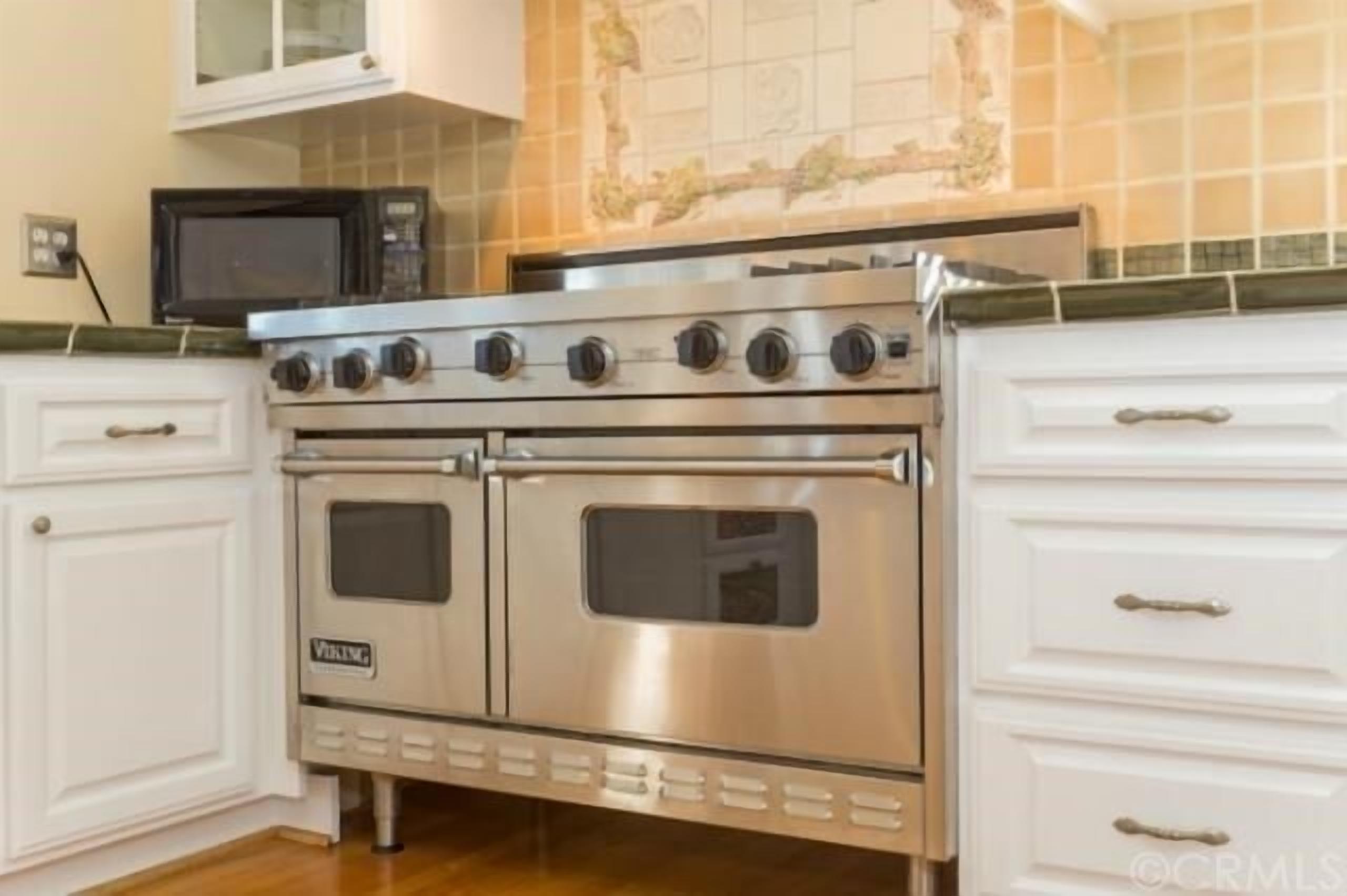Une cuisine équipée d’une cuisinière en acier inoxydable, de deux fours et de meubles de rangement blancs.