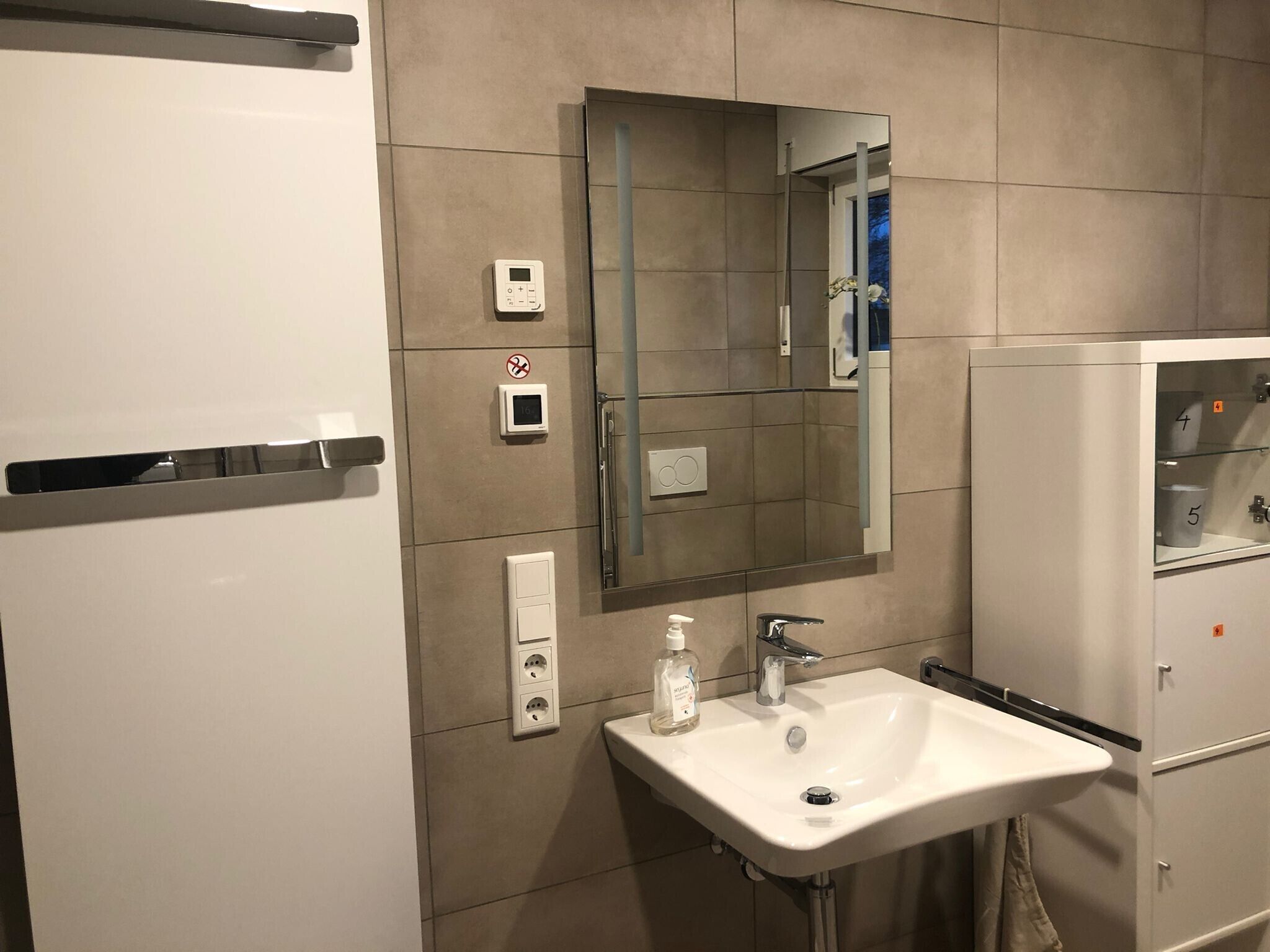 Un baño moderno con lavamanos, espejo y un armario blanco con puerta de vidrio.