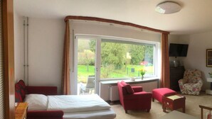 Ein Schlafzimmer mit großem Fenster, einem Bett, einem roten Sessel, einem kleinen Tisch und einem Fernseher.