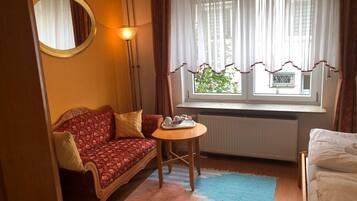 A cozy room with a sofa, a small table with cups and a tray, a window with curtains, and a radiator.