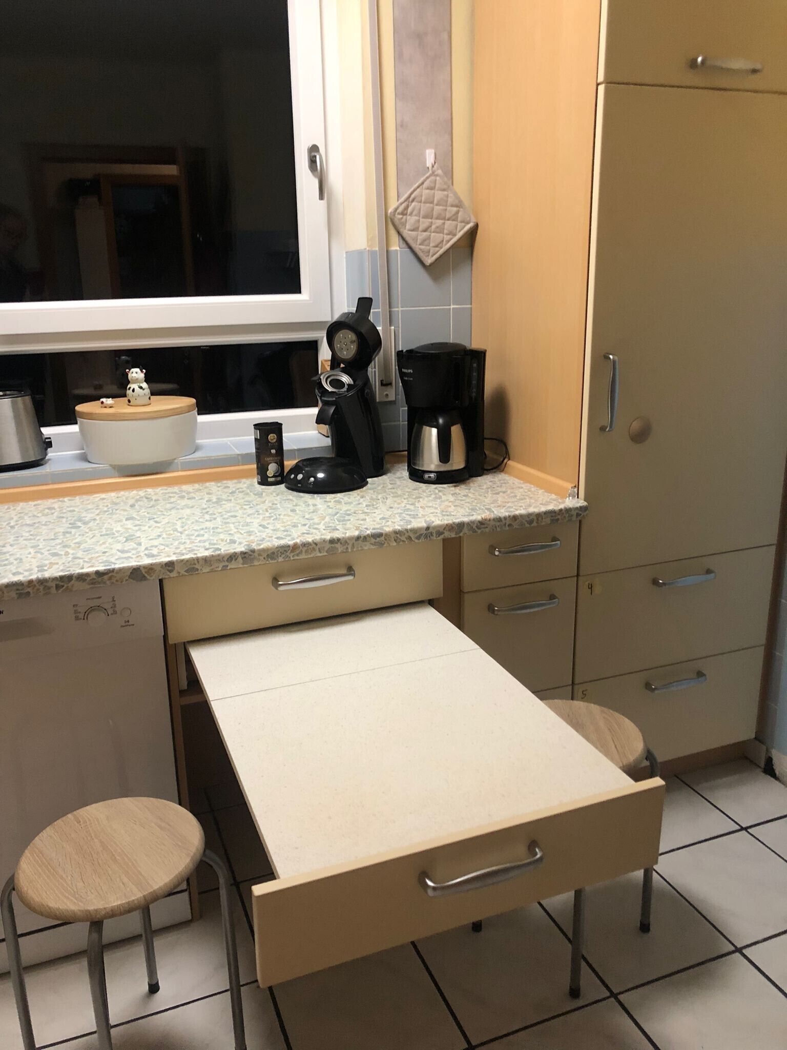 Et køkken med bordplade, kaffemaskine, elkedel og en lille pynteting.