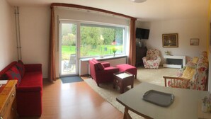 Ein Wohnzimmer mit einem roten Sofa, einem roten Sessel, einem blumengedeckten Sessel, einem Couchtisch und einem Fernseher an der Wand.