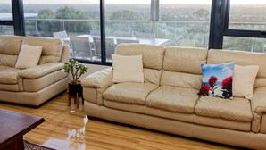 A spacious living area with a large window offering a city view. There are two beige sofas with cushions and a small table with a potted plant. - Magnificient Four Bedroom Home, Amazing Views (Baskerville)