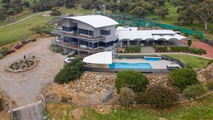 A modern two-story building with a pool, surrounded by landscaped gardens and a hilly backdrop. - Magnificient Four Bedroom Home, Amazing Views (Baskerville)