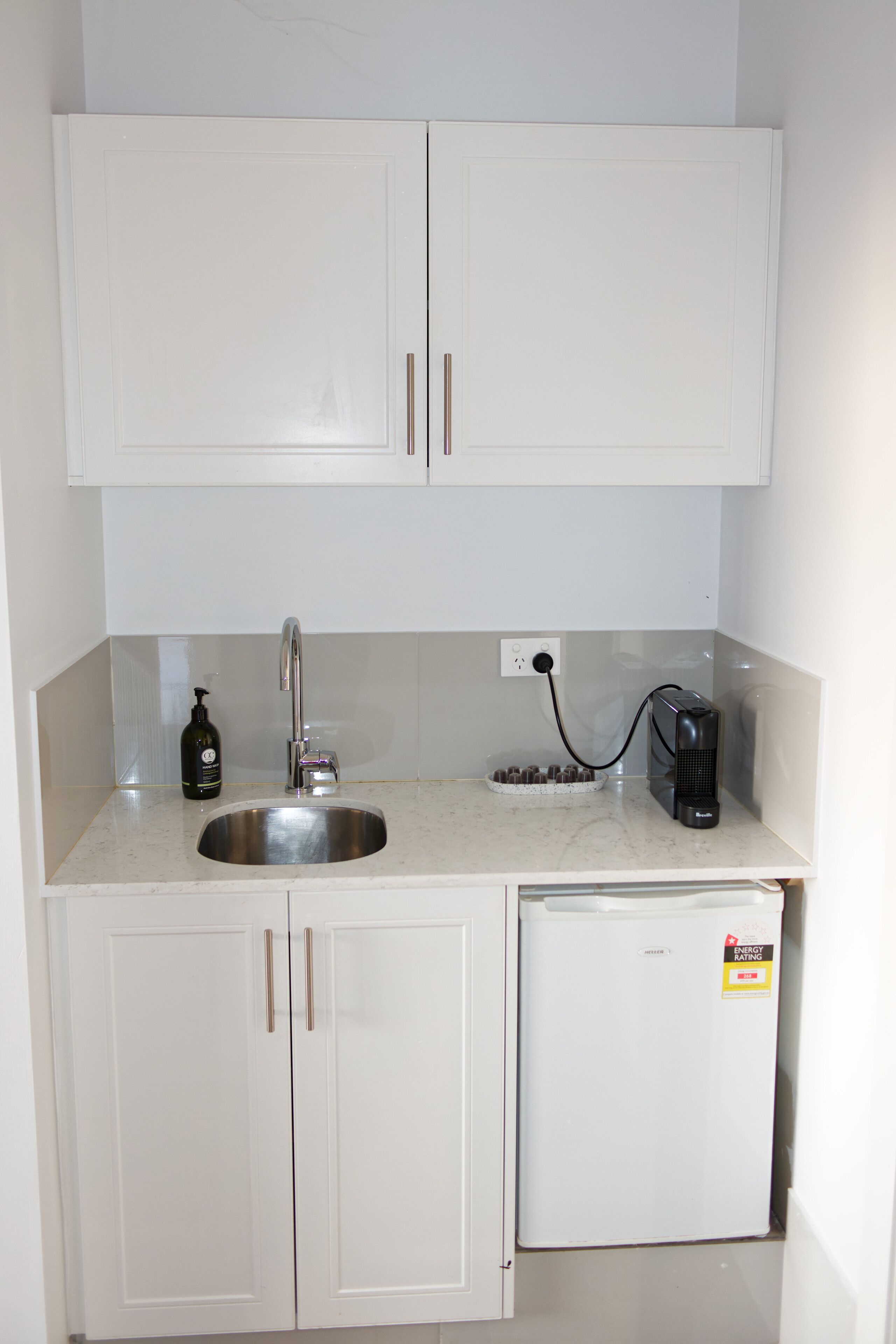 A compact kitchenette with a stainless steel sink, a small refrigerator, and a coffee maker.