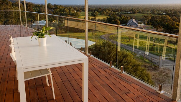A wooden deck with a white table and a potted plant, overlooking a rural landscape with houses and fields. - Magnificient Four Bedroom Home, Amazing Views (Baskerville)