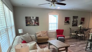 A living room with a sofa, armchair, coffee table, and a dining area with a table and chairs. - 3Br/2Ba Modern Bungalow w/ 6 Person Hot Tub! (Atlanta)