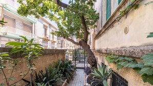 Un callejón estrecho con un árbol, plantas en macetas y una reja de metal.