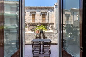 Un balcón con mesa y sillas, una planta en maceta y vistas a edificios históricos.