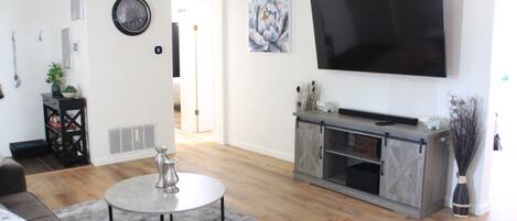 Una sala de estar moderna con un televisor de pantalla plana, una mesa de centro redonda, un sofá gris y una chimenea.