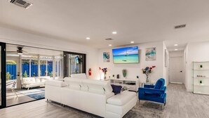 A modern living room with a white sofa, a blue armchair, and a TV mounted on the wall displaying a scenic ocean view. - Modern Spacious Home With Pool Jacuzzi (Fort Lauderdale)