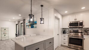 A modern kitchen with white cabinetry, stainless steel appliances, a marble island, and pendant lighting. - Modern Spacious Home With Pool Jacuzzi (Fort Lauderdale)