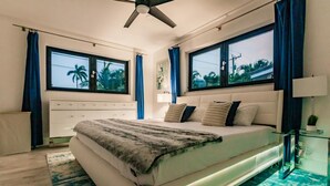 A modern bedroom with a large bed, two windows, a ceiling fan, and a nightstand with a lamp. - Modern Spacious Home With Pool Jacuzzi (Fort Lauderdale)