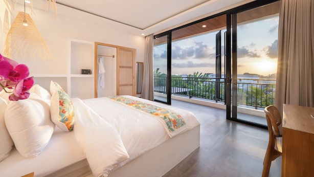 A modern bedroom with a large bed, a wooden desk, and a balcony with a view of the city. - Villa Greenland Canggu by Nagisa Bali (Canggu)