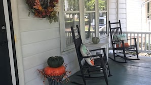 Une véranda avec deux fauteuils à bascule, une guirlande et des citrouilles.