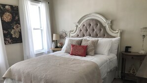 Un lit bien fait, avec une tête de lit blanche, un coussin rouge vif et une courtepointe blanche.