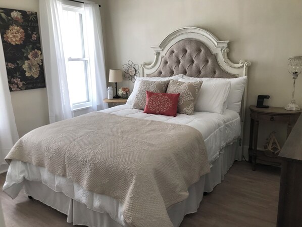 A neatly made bed with a white headboard, a red accent pillow, and a white quilt.