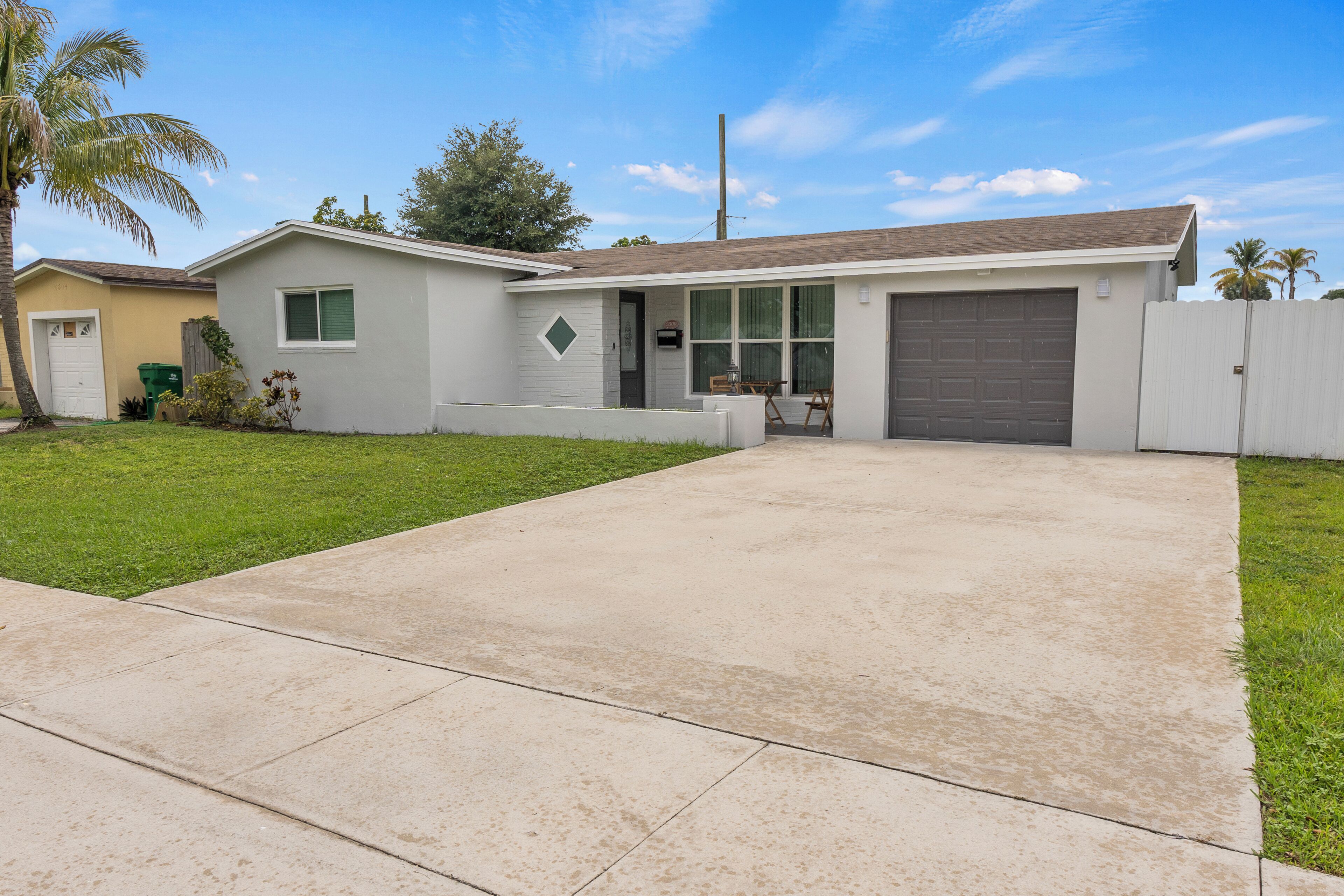 A single-story house with a garage, a front lawn, and a palm tree.